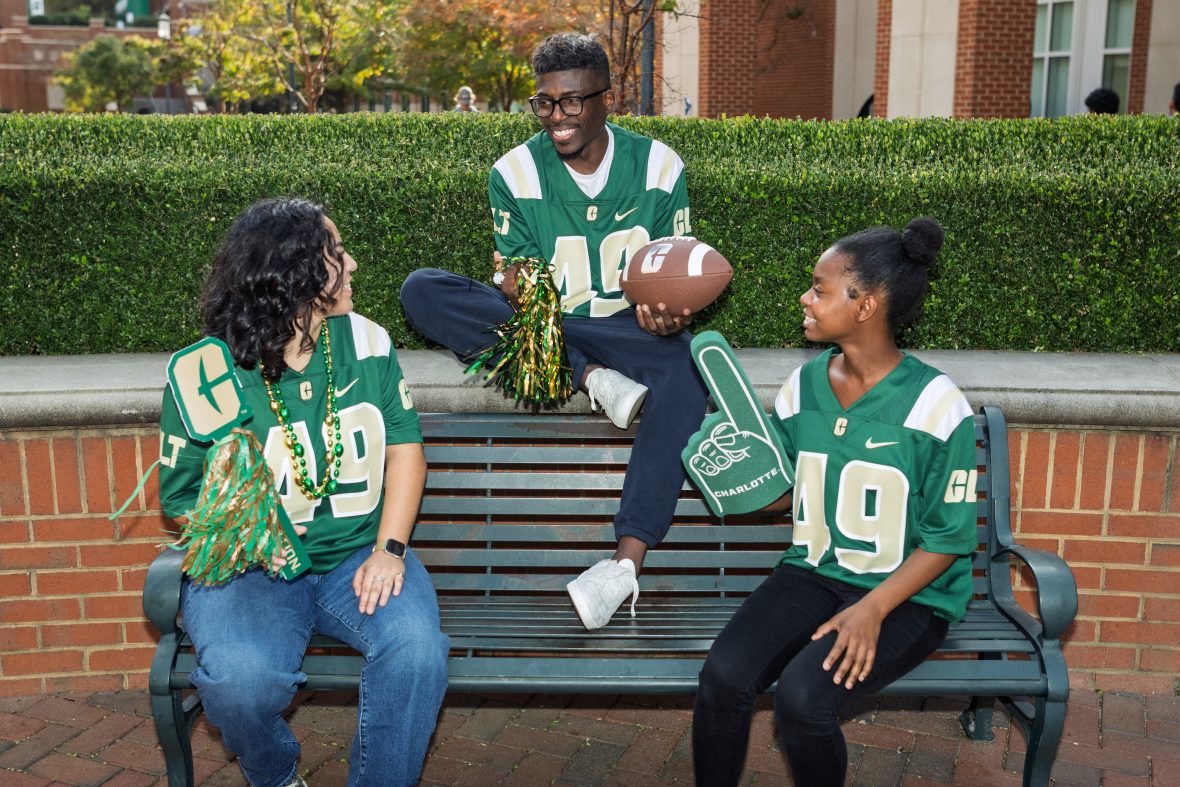 Students wearing Charlotte 49ers merchandise sitting on bench outside.