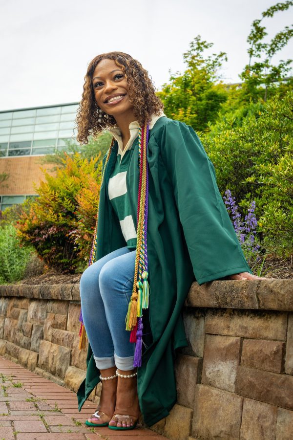 student wearing a green commencement gown poses in front of the fountain
