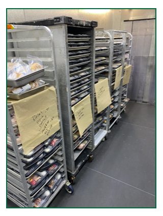Photo of racks of meals, stacked and ready for delivery in a walk-in refrigerator