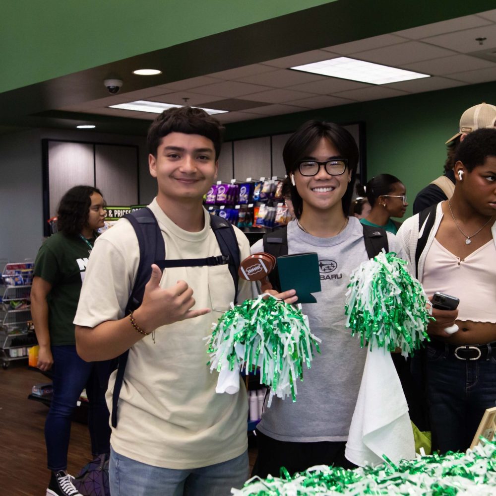 Two students pose with picks-up hand signs and green and white pom poms in Charlotte Barnes & Noble