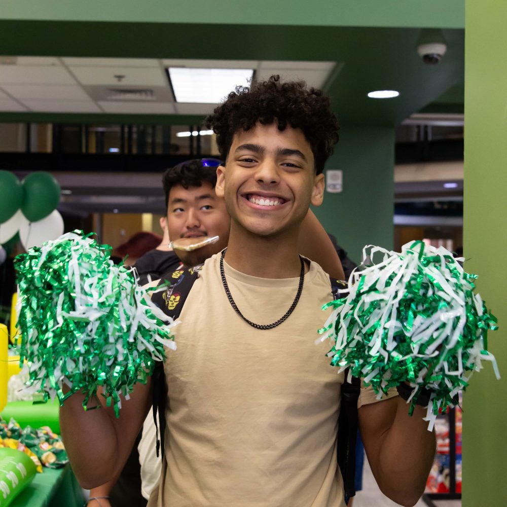 Student poses with big smile and green and white pom poms in Charlotte Barnes & Noble