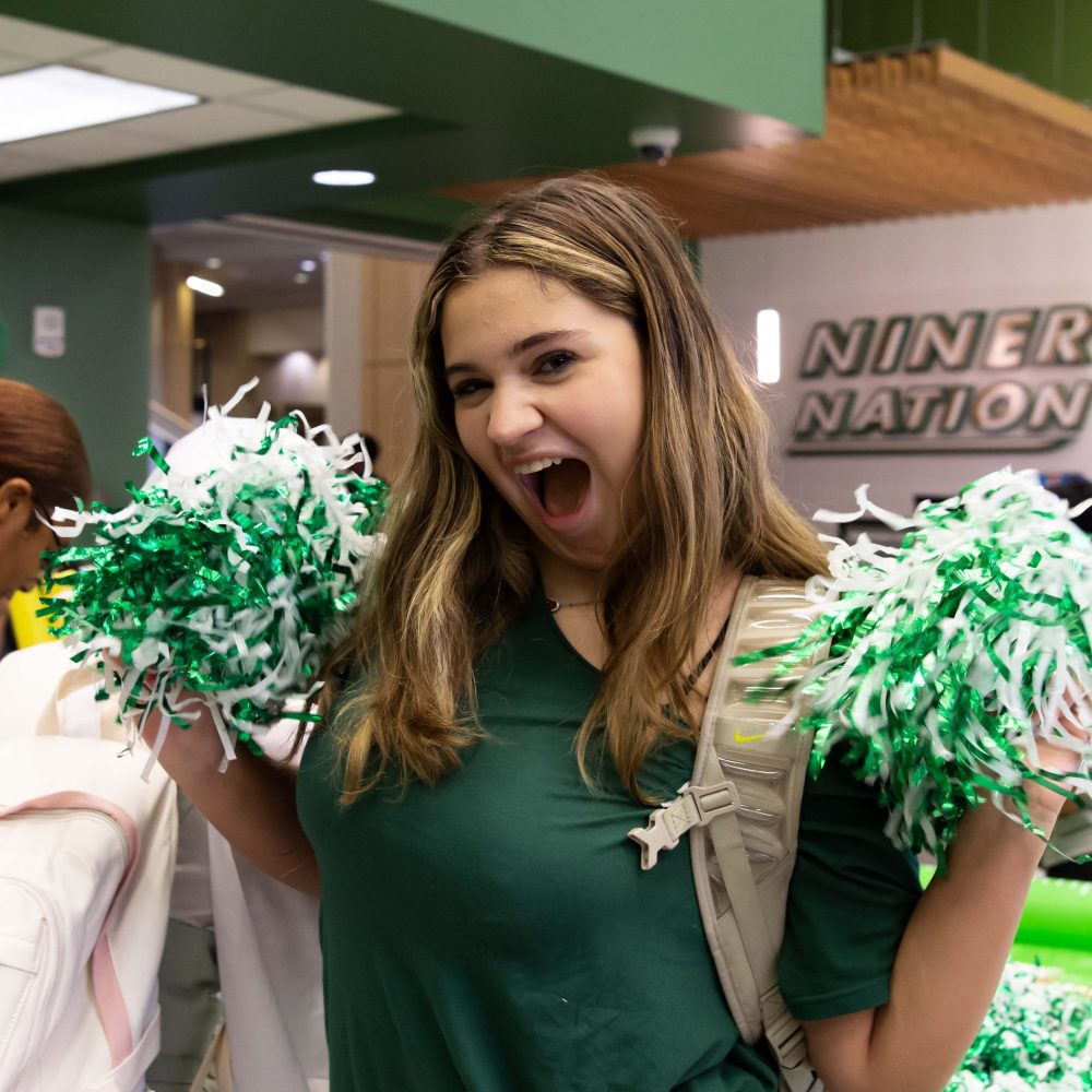 Student cheers with green and white pom poms in Charlotte Barnes & Noble