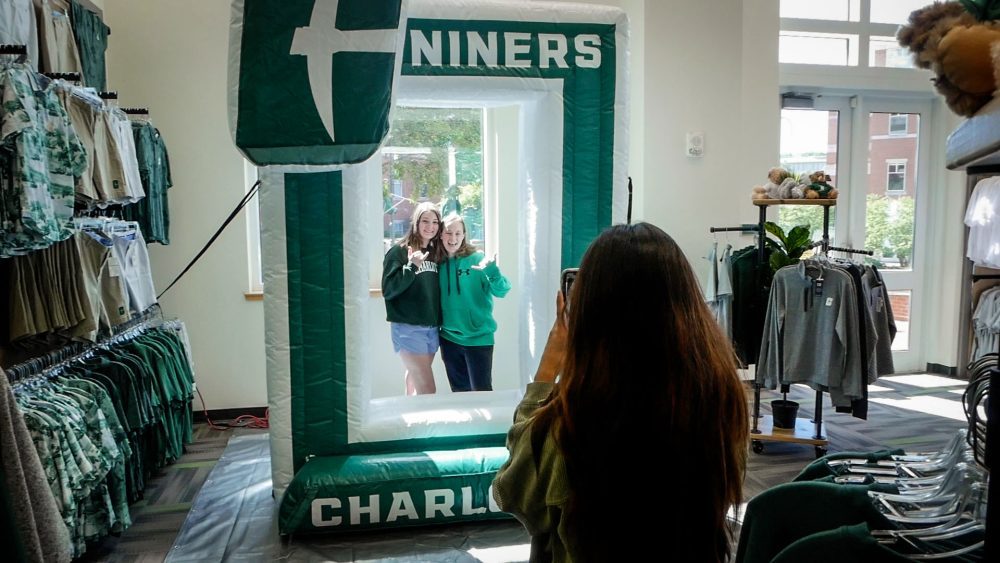 Two smiling students pose for a photo with an inflatable Niners Charlotte frame
