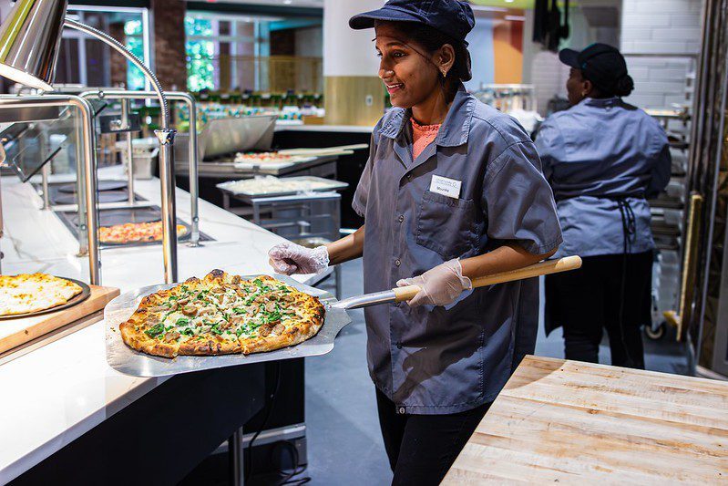 A staff member pulls a hot pizza out of the oven to serve