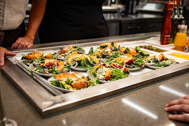 A row of delicious-looking peach and feta salads line the serving station