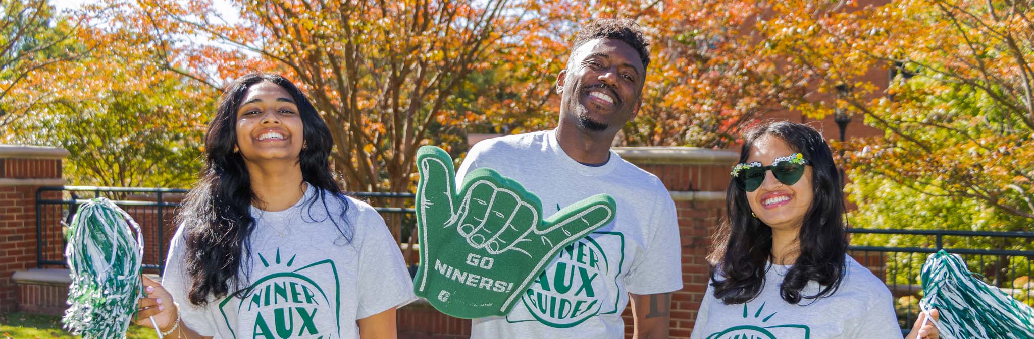 Niner Aux Guides smiling and holding poms poms and a foam finger.
