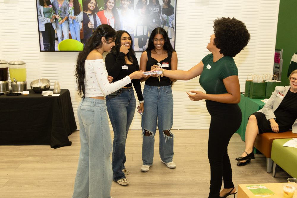 Niner Aux Guide co-lead Natalia Harris hands 3 musketeers chocolate bars to laughing Sarmitha Rajesh Kumar, Sowmya Ravuri and Yeshritha Gelle.