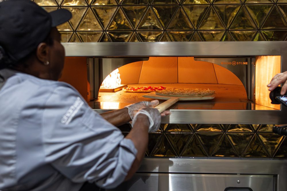 Dining Hall culinary assistant pushes dough into pizza oven