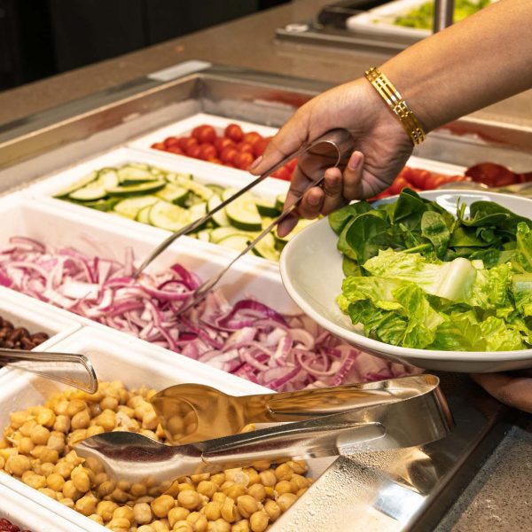 Hand holding tongs at a salad bar.