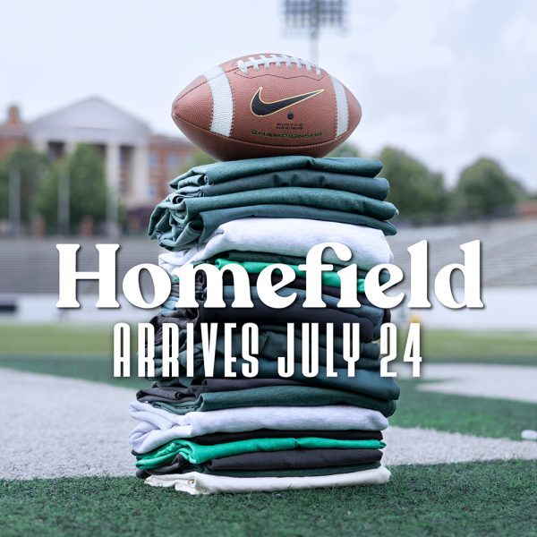 Homefield logo with text "Arrives July 24" overlays a picture of a football sitting on a neatly stacked pile of green and white shirts in the Charlotte football stadium