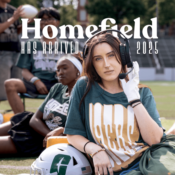 young woman poses on a football field in Homefield tshirt in front of text "Homefield has arrived 2025"