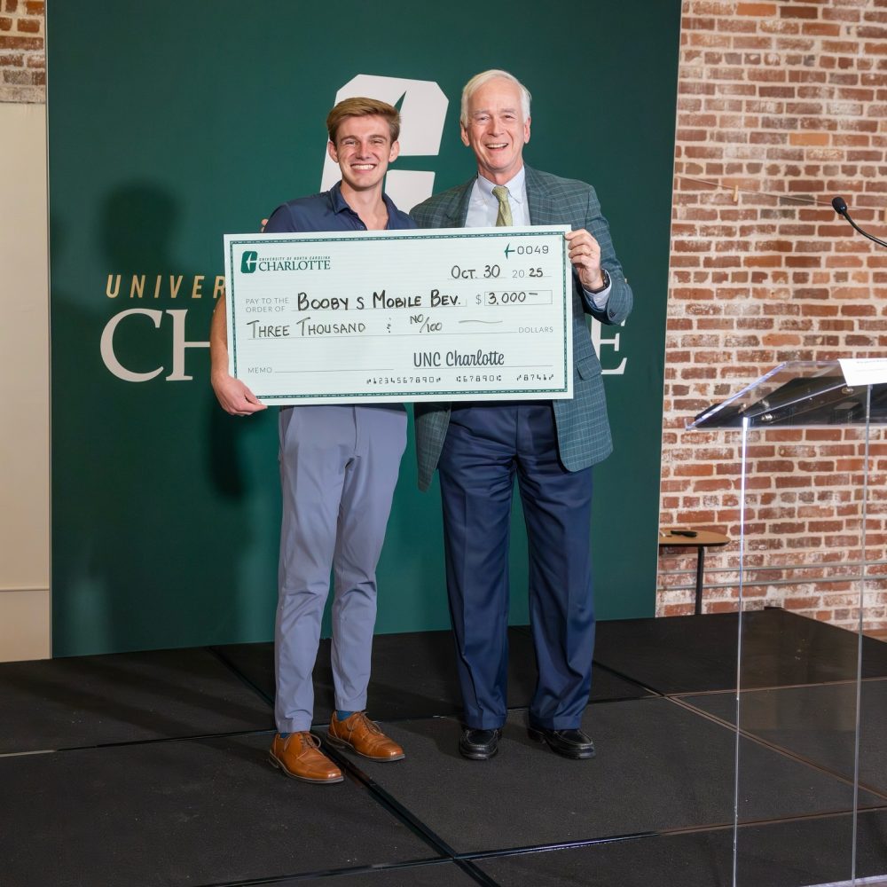 UNC Charlotte representative hands Nicholas Huger a jumbo check for $3000 made out for Boobys Mobile Bev